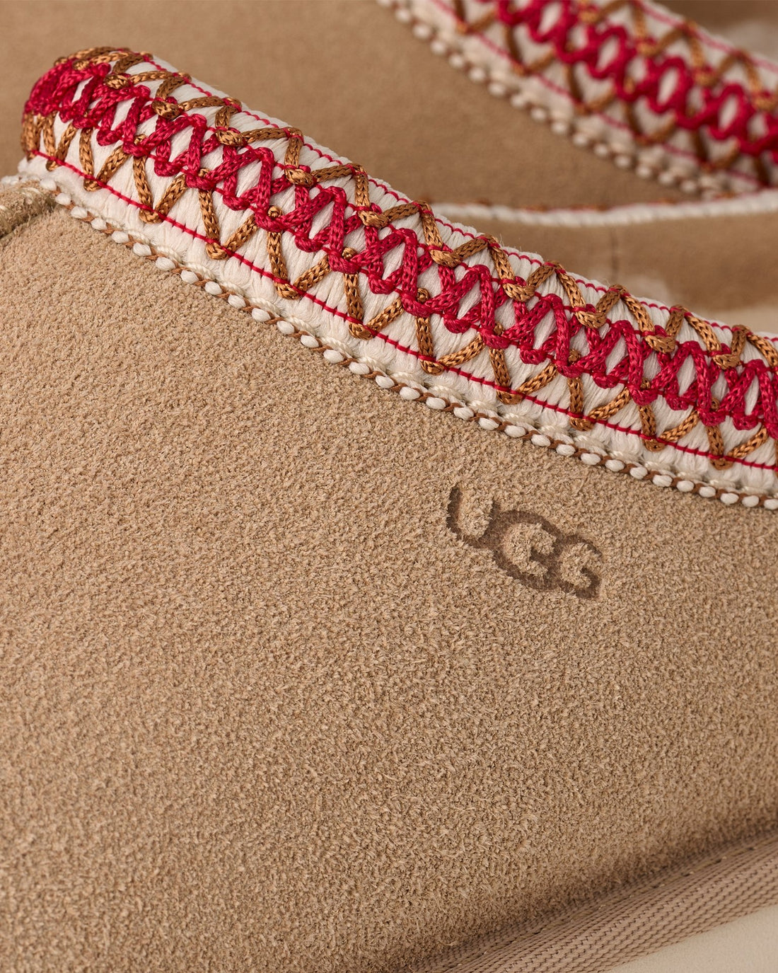 Close-up of a UGG shoe with embroidered strap on a beige background